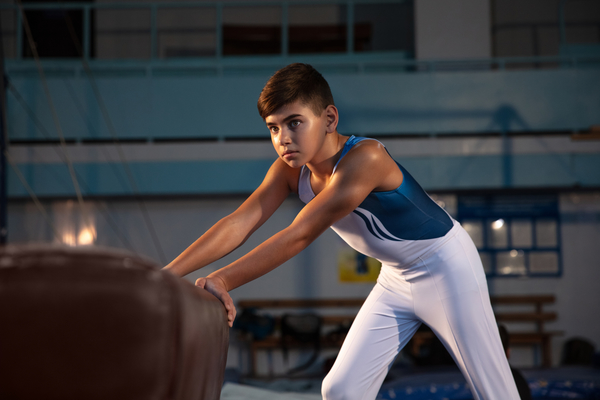 Little male gymnast training in gym, flexible and active. Caucasian fit little boy, athlete in white sportswear preparing for exercises for strength, balance. Movement, action, motion, dynamic concept.
